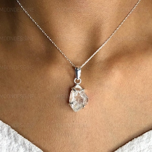 Puede incluir: Un collar de cadena de plata con un colgante de cristal de cuarzo transparente. El cristal es en bruto y tiene una forma natural irregular.