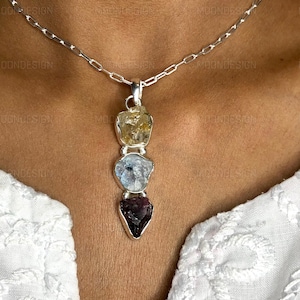 May include: A silver chain necklace with a pendant featuring four raw gemstones in a graduated size. The stones are yellow, blue, and purple.