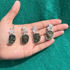 May include: Four silver pendants featuring green and clear stones. Each pendant has a green stone with a clear stone on top. The pendants are shown on a hand.