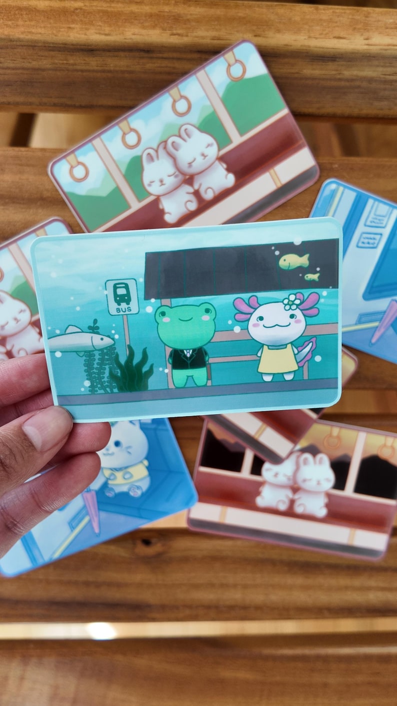 K&ouml;nnte beinhalten: Eine Sammlung farbenfroher Aufkleber mit niedlichen Cartoon-Charakteren. Ein Aufkleber zeigt einen Frosch im Anzug und einen Axolotl in einem gelben Kleid. Andere Aufkleber zeigen Hasen und Busszenen. Die Aufkleber sind rechteckig mit abgerundeten Ecken.