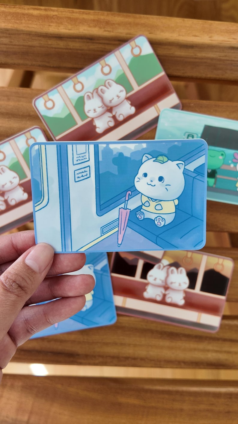 K&ouml;nnte beinhalten: Eine Sammlung farbenfroher Aufkleber mit Cartoon-Tieren. Ein Aufkleber zeigt eine wei&szlig;e Katze mit gr&uuml;nem Hut und rosa Regenschirm. Weitere Aufkleber zeigen Hasen und einen Frosch. Die Aufkleber haben eine gl&auml;nzende Oberfl&auml;che.