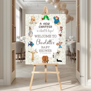 May include: A wooden easel displays a baby shower welcome sign. The sign features the text "A New Chapter is about to begin! Welcome to Charlotte's Baby Shower" with illustrations of storybook characters. The background has a floral pattern.