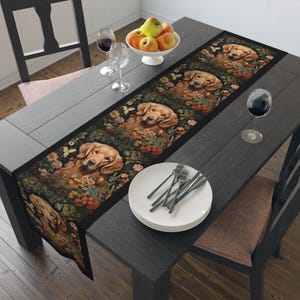 May include: A black table runner with a floral pattern and images of golden retrievers. The runner is on a dark wood table with a bowl of apples, wine glasses, and a plate of silverware.