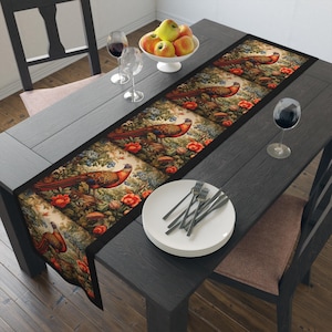 Puede incluir: Camino de mesa rectangular con un diseño detallado de faisanes y borde negro, colocado sobre una mesa de madera oscura. La escena incluye platos, cubiertos y copas de vino, sugiriendo un ambiente de comedor.