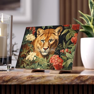 May include: A close-up of a painting featuring a large, orange-brown cougar with green eyes, peering out from behind a lush, green jungle with red and white flowers.
