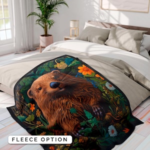 May include: A fleece blanket with a brown and black otter surrounded by green leaves and colorful flowers. The otter is looking at the camera with a friendly expression.