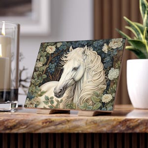May include: A white horse with a long flowing mane stands in a lush garden setting. The horse's head is turned to the side, and its eyes are closed. The background is filled with green leaves and white flowers.