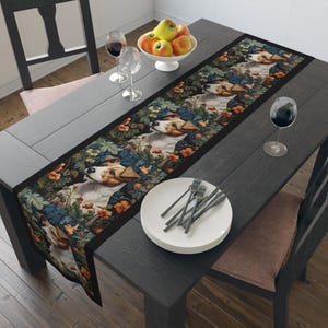 May include: A black table runner with a repeating pattern of Jack Russell terriers in a floral setting. The runner is on a dark wood table with a bowl of apples, two wine glasses, and a set of silverware.