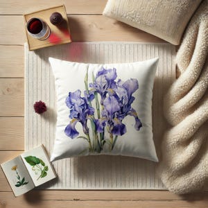 May include: A white pillow with a watercolor illustration of purple irises. The pillow is on a white textured surface.