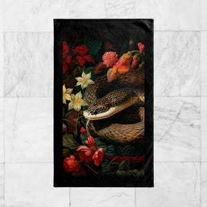 May include: A black and brown snake wrapped around a bouquet of red, pink, and white flowers. The snake's head is visible, and its eyes are open. The flowers are arranged in a lush, tropical setting.