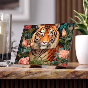 May include: A square wooden art print featuring a detailed illustration of a tiger surrounded by lush greenery and pink flowers. The tiger has orange and black stripes with piercing blue eyes. The print is displayed on a wooden stand.