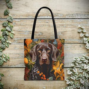 May include: A brown and white German Shorthaired Pointer dog with a floral background. The dog is looking directly at the viewer. The tote bag is black with a white handle.
