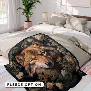 Op de afbeelding: Een fleece deken met een close-up afbeelding van een wolvenkop omringd door weelderig groen gebladerte en witte bloemen. De wolf heeft een bruine en bruine vacht met doordringende gele ogen. De achtergrond is donker zwart.