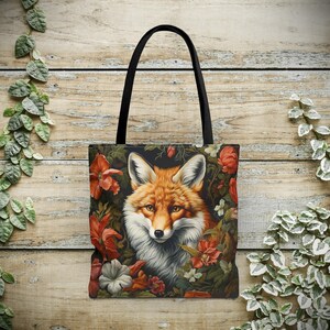 Puede incluir: Una bolsa de lona negra con una ilustración colorida de un zorro rodeado de flores. El zorro tiene un pelaje naranja, un pecho blanco y ojos negros.