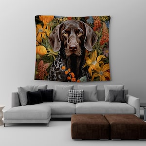 May include: A brown and white German Shorthaired Pointer dog with a black nose and brown eyes is surrounded by colourful flowers. The dog is looking directly at the viewer. The background is a dark green.