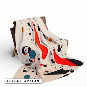 May include: A white fleece blanket with a colourful abstract design featuring red, black, blue, and yellow shapes. The design is reminiscent of modern art.