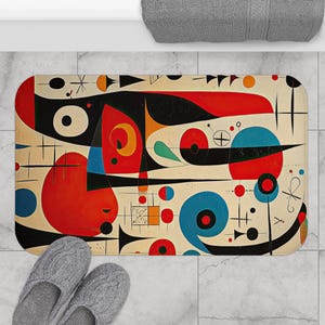 May include: Abstract art bath mat with a white background and geometric shapes in red, blue, black, and yellow.