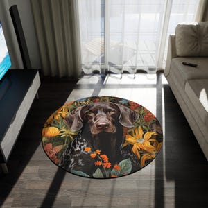 Könnte beinhalten: Runder Teppich mit einem Deutsch Kurzhaar Hund, umgeben von bunten Blumen. Der Teppich hat einen schwarzen Rand und liegt auf einem Holzboden. Das Fell des Hundes ist braun mit weißen Flecken.