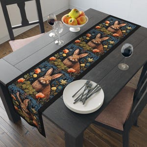 May include: A black table runner with a repeating pattern of rabbits, flowers, and leaves. The runner has a dark blue background with gold accents.