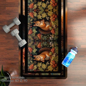 May include: A black and brown yoga mat with a repeating pattern of red berries, green leaves, and squirrels. The text "MAT OPTION: Rubber 26 X 70" is printed on the bottom of the mat.
