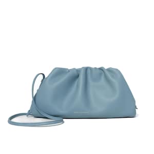 Può includere: Una pochette in pelle blu polvere con apertura superiore arricciata e una sottile tracolla abbinata. La parte anteriore della borsa presenta il testo dorato FREYA ESTEPHAN centrato vicino al bordo inferiore, mostrando una silhouette morbida.