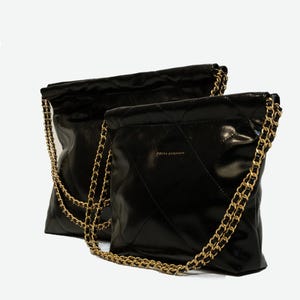 Puede incluir: Dos bolsos negros acolchados con correas de cadena doradas. Los bolsos tienen un acabado brillante y un patr&oacute;n de diamantes. El nombre de la marca "FREYA ESTHERMAN" est&aacute; impreso en dorado en la parte delantera de un bolso.
