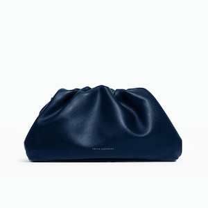 Könnte beinhalten: Eine dunkelmarineblaue Clutch mit einem weichen, gerafften und gefalteten Design an der Oberseite. Die Tasche hat eine glatte, matte Oberfläche und einen rechteckigen Boden. Der Text FREYA ESTEPHAN ist in kleinen, hellen Großbuchstaben unten mittig.