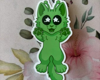 May include: A green sticker featuring a cartoon alien cat with star-shaped eyes and paw prints. The alien cat has antennae and is smiling with its paws up. The sticker is on a floral background.