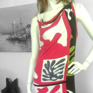 Peut inclure: Une robe sans manches avec un col en V et un motif géométrique dans des tons de rose, blanc, noir et vert. La robe est ample et fluide.