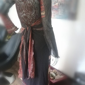 Könnte beinhalten: Ein langes, schwarzes Kleid mit vertikalen Streifen und einem gemusterten Rücken. Das Kleid hat lange Ärmel mit ausgestellten Manschetten und einen dekorativen Schärpe, die in der Taille gebunden ist. Der Saum hat ein rosa-weißes Blumenmuster.