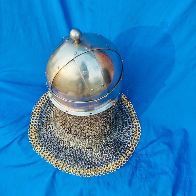 May include: A silver helmet with a chainmail coif. The helmet has a rounded top and a decorative band around the base. The coif is made of interlocking metal rings.