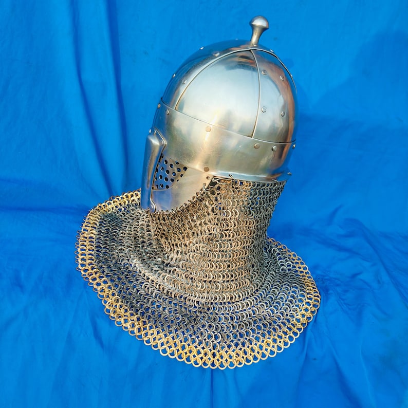 May include: A silver helmet with a chainmail coif. The helmet has a pointed top and a face mask with a small opening for the eyes. The coif is made of interlocking metal rings.