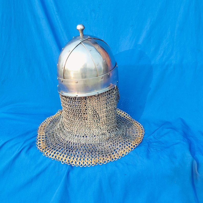 May include: A silver helmet with a chainmail coif. The helmet has a rounded top and a pointed tip. The chainmail coif is made of small metal rings linked together.