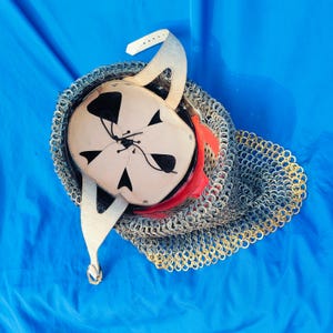 May include: A medieval helmet with a chainmail coif. The helmet is made of metal and has a leather lining. The coif is made of metal rings linked together.