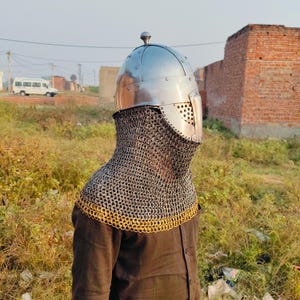 May include: A silver helmet with a chainmail coif. The helmet has a pointed top and a face mask with a small opening for the eyes. The coif is made of small metal rings linked together.