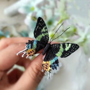 May include: A handmade butterfly with black wings, featuring green, blue, and orange patterns. The butterfly's wings are finely detailed, and the antennae are slender and wire-like. The butterfly is a decorative item.