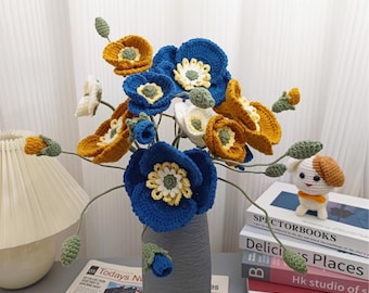 May include: A bouquet of handmade crochet flowers in a gray vase. The flowers are in shades of blue, yellow, and white, with green stems and leaves. A small crochet dog figurine sits beside a stack of books. The newspaper on the table reads "Todays News".