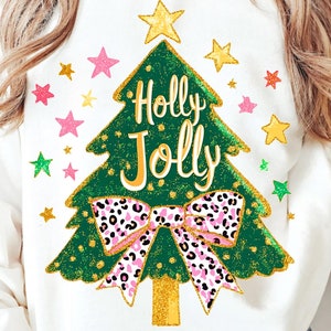 May include: White sweatshirt featuring a green Christmas tree design with the words "Holly Jolly" in white. The tree has a gold star on top and a pink and black leopard print bow. Colorful stars surround the tree.