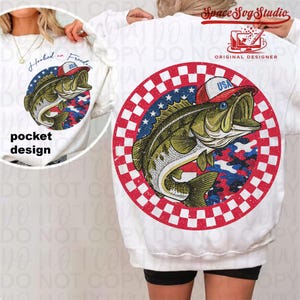 May include: White sweatshirt featuring a graphic of a fish wearing a red, white, and blue hat. The fish is set against a camouflage pattern and a red and white checkered border. The text "Hooked on Freedom" is on the pocket design.