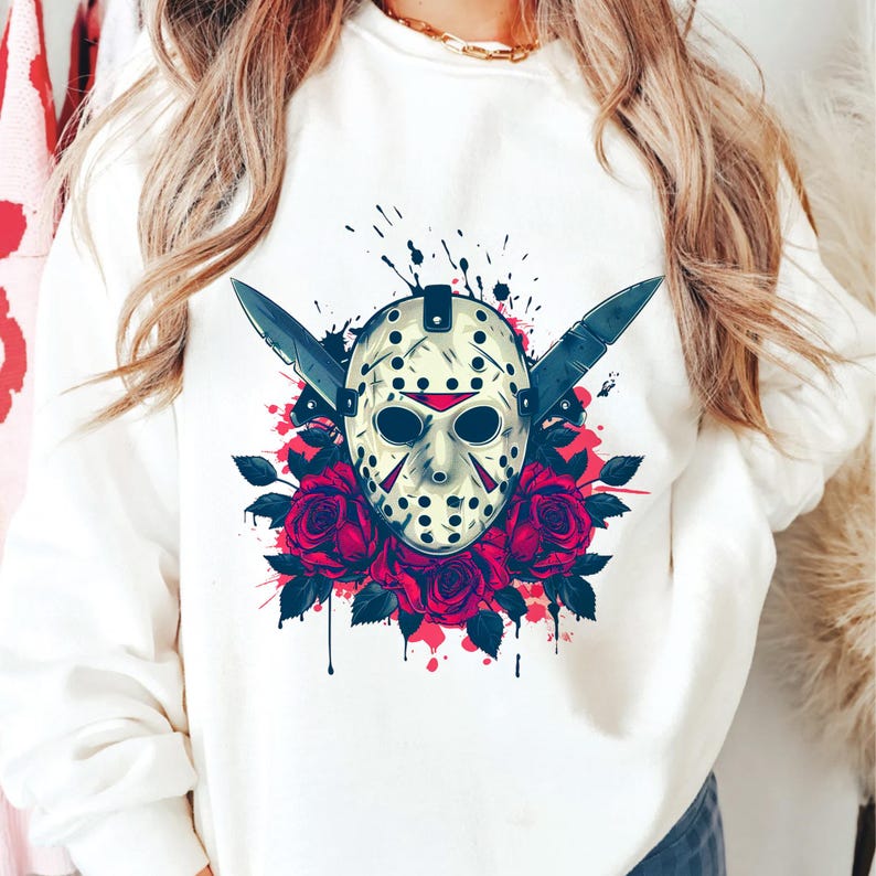 Peut inclure: Sweat-shirt blanc avec un motif graphique. Le motif repr&eacute;sente un masque de hockey, deux couteaux et des roses rouges. Le masque est de couleur cr&egrave;me avec des accents noirs et des d&eacute;tails rouges. Les roses sont d'un rouge profond.