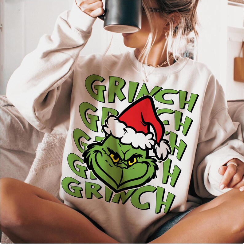 Puede incluir: Una sudadera color crema con la cara verde del Grinch con un gorro de Pap&aacute; Noel rojo con ribete blanco. La palabra "GRINCH" est&aacute; impresa en verde varias veces alrededor de la cara del Grinch. Es un art&iacute;culo festivo de vacaciones.