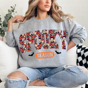May include: A gray sweatshirt with the word "SPOOKY" in a floral design with clown faces. The word "SEASON" is below in an orange oval, with black bat graphics.