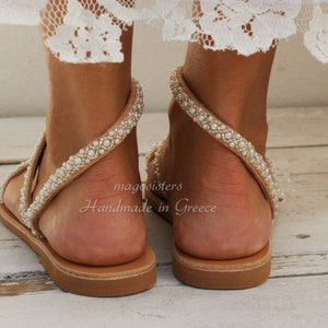 May include: Tan leather sandals with a beaded strap and a flat sole. The sandals are handmade in Greece.