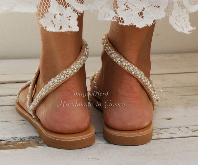 May include: Tan leather sandals with a beaded strap and a flat sole. The sandals are handmade in Greece.