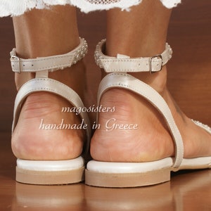 May include: White leather sandals with a beaded ankle strap and a buckle closure. The sandals are handmade in Greece and have a white leather sole.