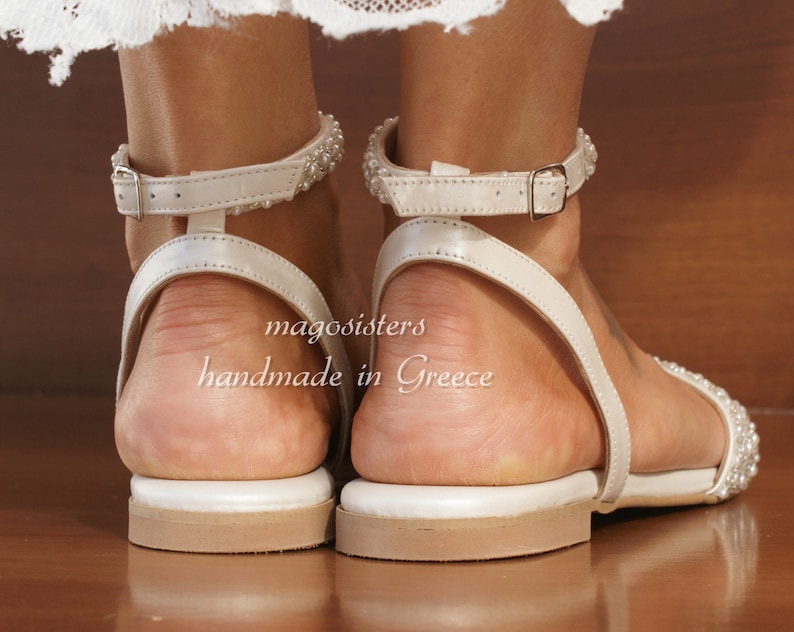 May include: White leather sandals with a beaded ankle strap and a buckle closure. The sandals are handmade in Greece and have a white leather sole.