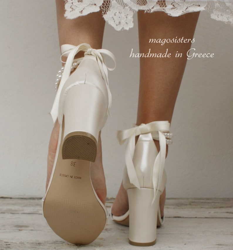 Puede incluir: Tacones de novia de sat&eacute;n marfil con un tac&oacute;n de bloque grueso y adornos de perlas. Los tacones tienen un lazo de sat&eacute;n para atar en el tobillo y est&aacute;n etiquetados como "Made in Greece 38".