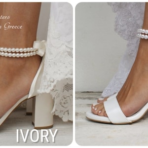 Puede incluir: Dos pares de tacones de novia blancos con correas de tobillo de perlas y lazos de sat&eacute;n. Los tacones est&aacute;n disponibles en marfil y blanco.