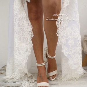 Puede incluir: Sandalias de novia de sat&eacute;n blanco con tiras de tobillo de perlas. Las sandalias tienen un delicado lazo de cinta en el tobillo. El texto "magnolisters handmade in Greece" es visible en la imagen.