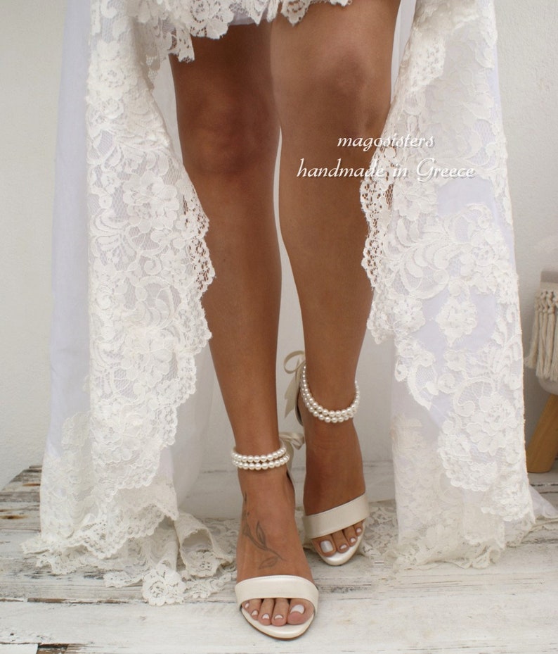 Puede incluir: Sandalias de novia de sat&eacute;n blanco con tiras de tobillo de perlas. Las sandalias tienen un delicado lazo de cinta en el tobillo. El texto "magnolisters handmade in Greece" es visible en la imagen.